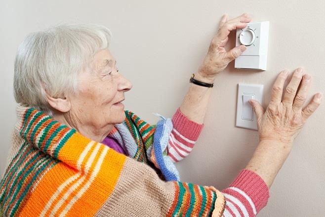 Image: woman turning the thermostat up to 18 degrees